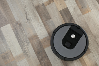 Modern robotic vacuum cleaner on wooden floor, top view. Space for text