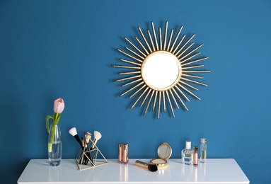 Photo of Dressing table with spring flower and makeup products at blue wall