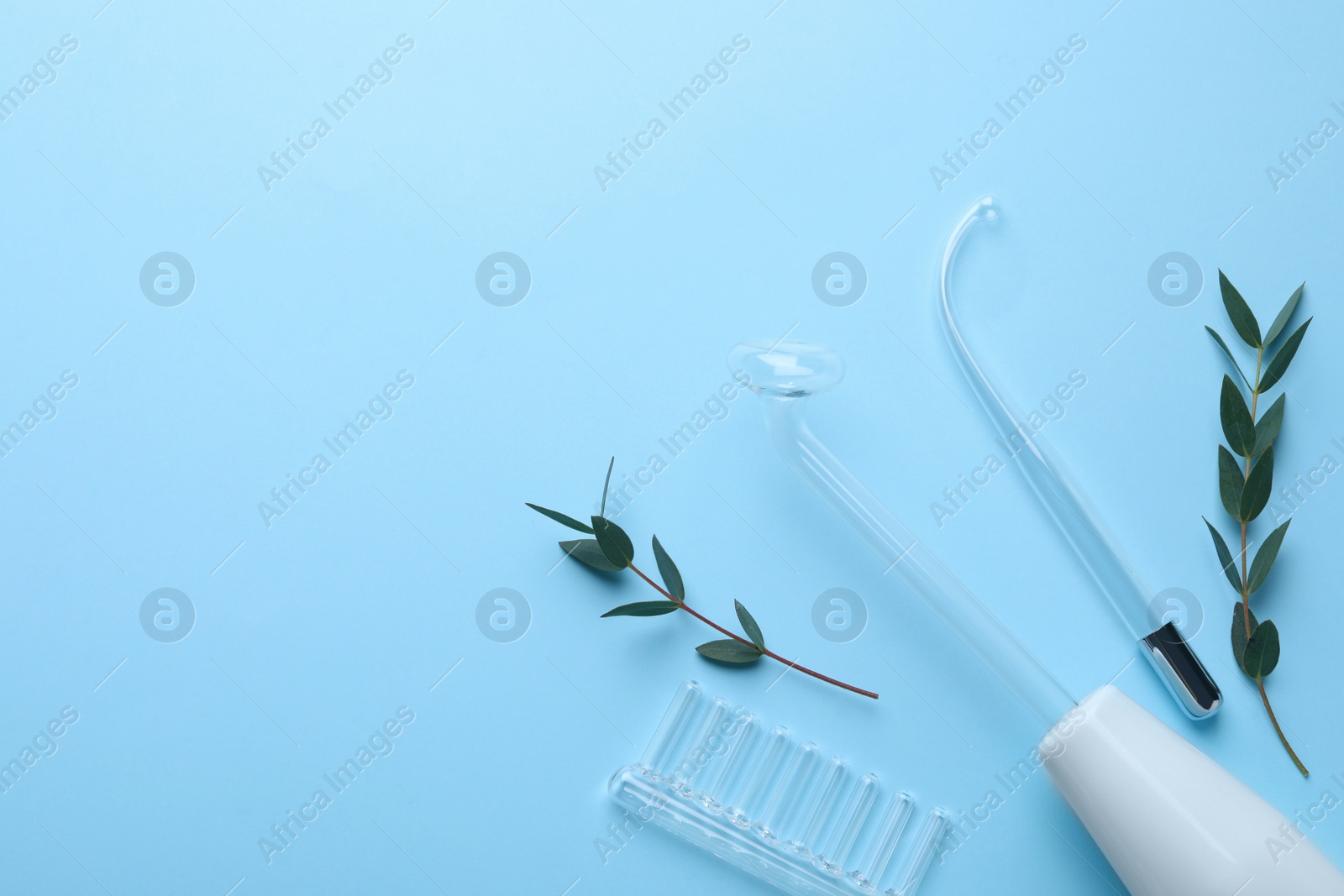 Photo of Modern darsonval with nozzles and tree branches on light blue background, flat lay. Space for text