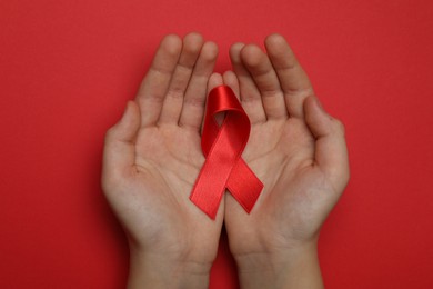 Photo of Little girl holding red ribbon on bright background, top view. AIDS disease awareness