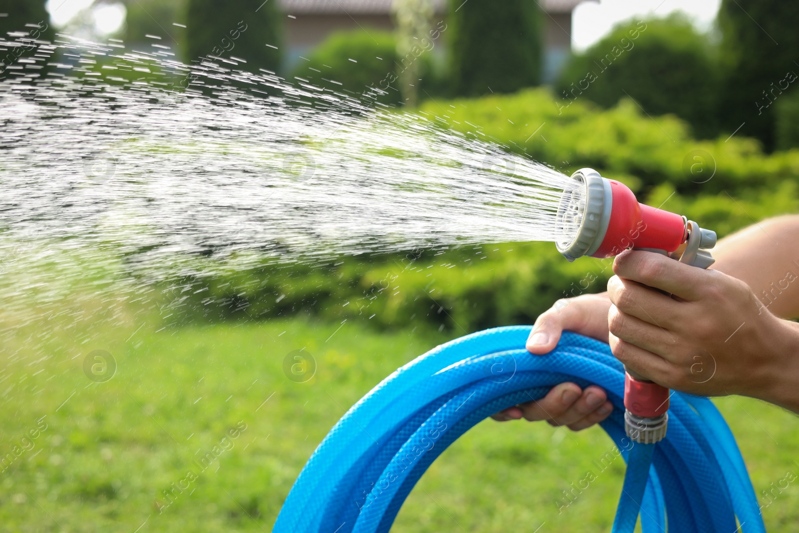 Photo of Man spraying water from hose in garden, closeup