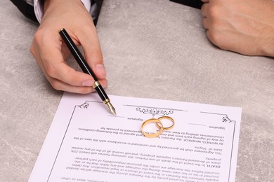 Man signing marriage contract at light grey table, closeup