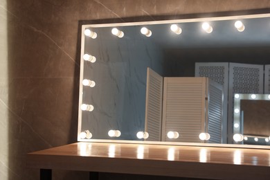 Photo of Modern mirror with light bulbs on wooden table in room