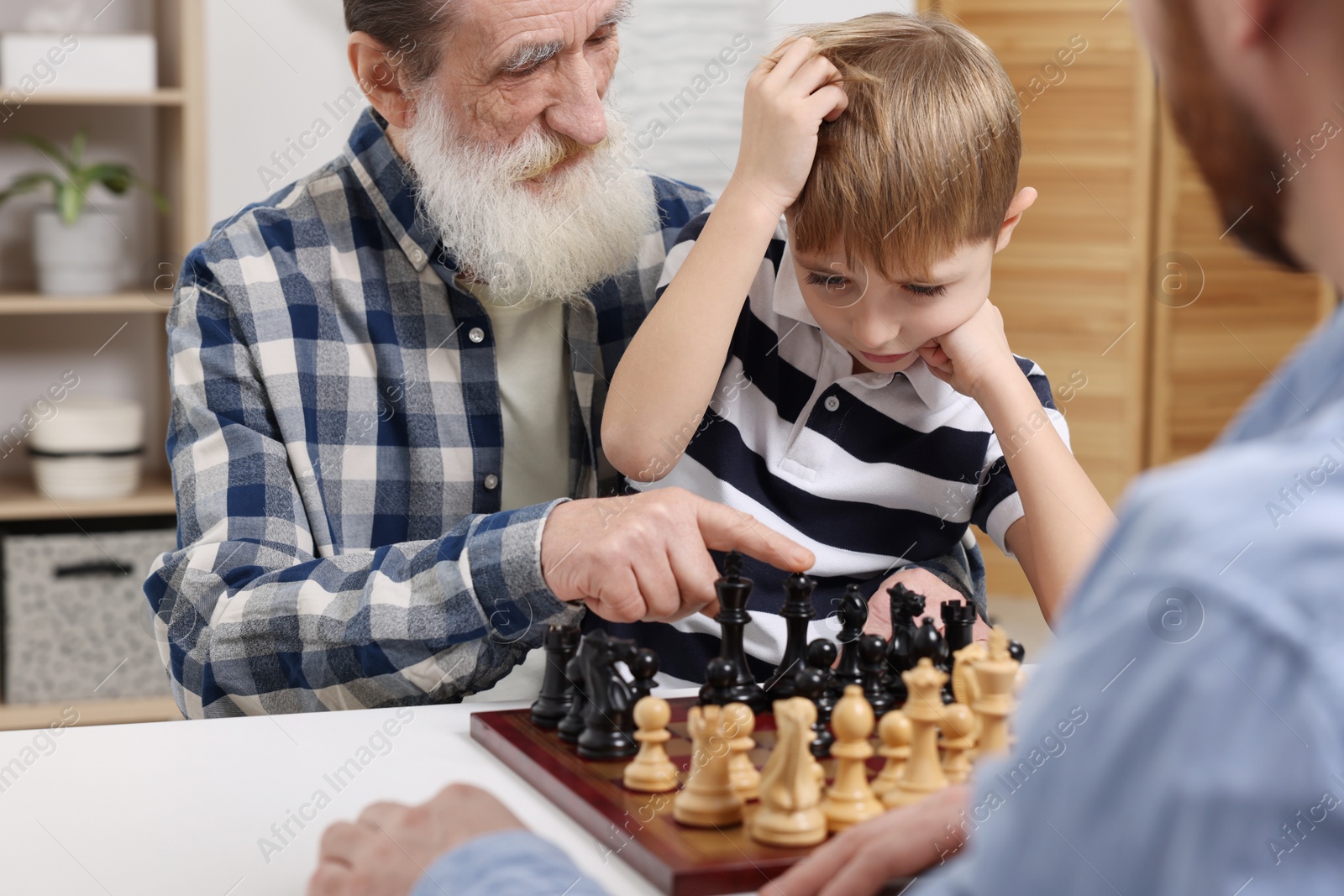 Photo of Family playing chess together at table in room