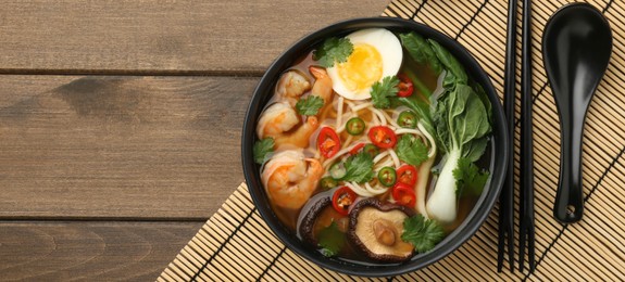 Photo of Delicious ramen with shrimps and egg in bowl served on wooden table, flat lay with space for text. Noodle soup