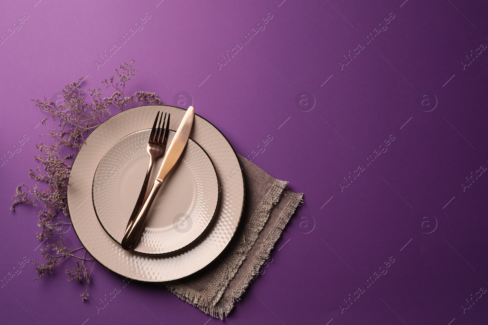 Photo of Stylish table setting. Plates, cutlery, napkin and floral decor on purple background, top view with space for text