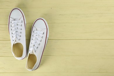 Photo of Pair of white sneakers on yellow wooden table, flat lay. Space for text