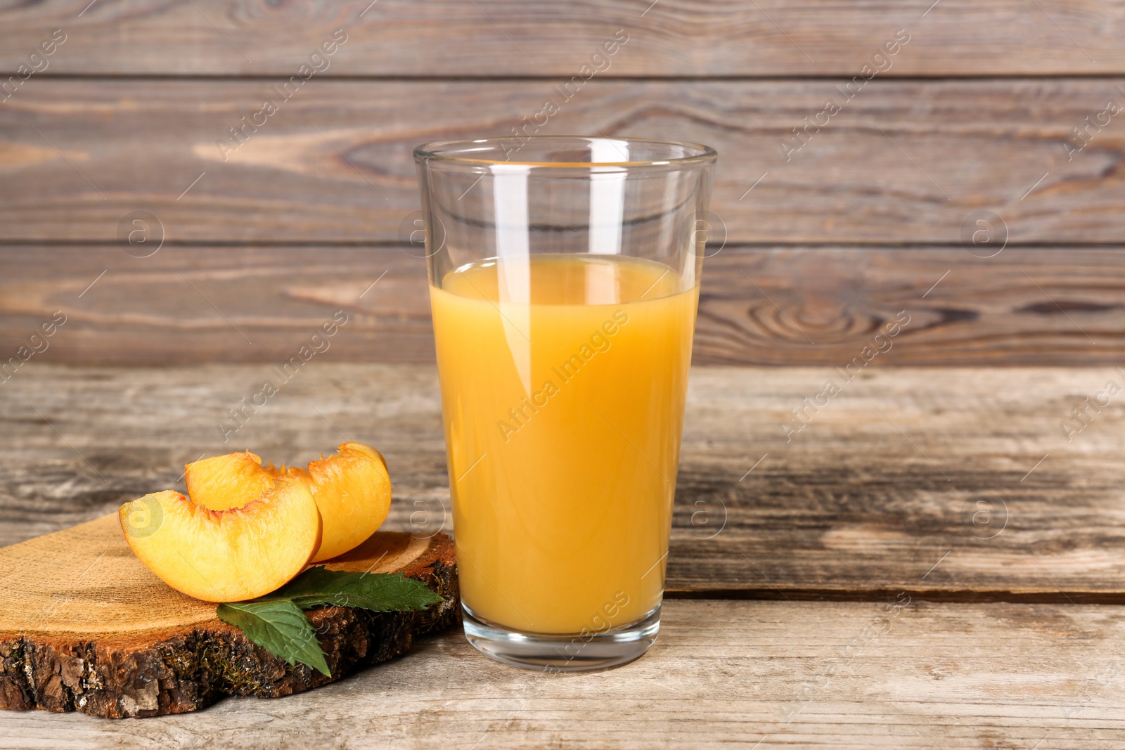 Photo of Glass of delicious peach juice, cut fresh fruit and leaves on wooden table