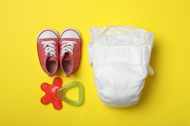 Photo of Diaper, child's shoes and teether on yellow background, flat lay