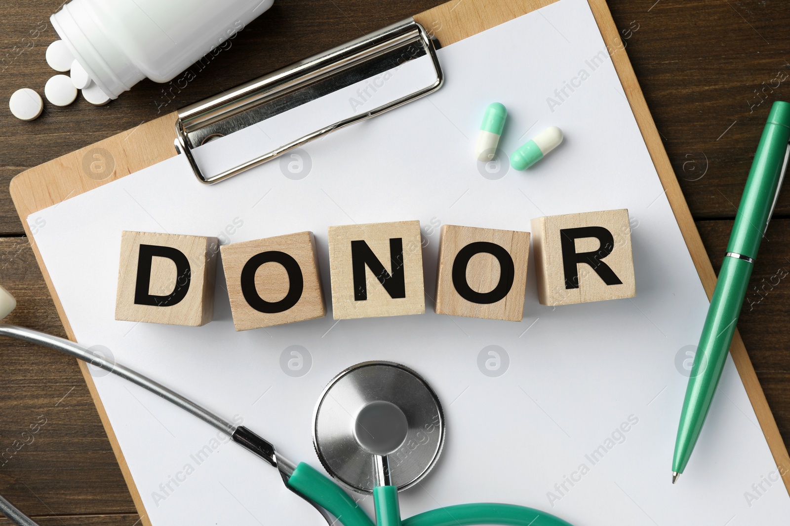 Photo of Word Donor made of cubes, clipboard, stethoscope and pills on wooden table, flat lay