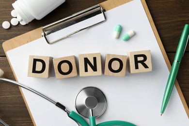 Word Donor made of cubes, clipboard, stethoscope and pills on wooden table, flat lay