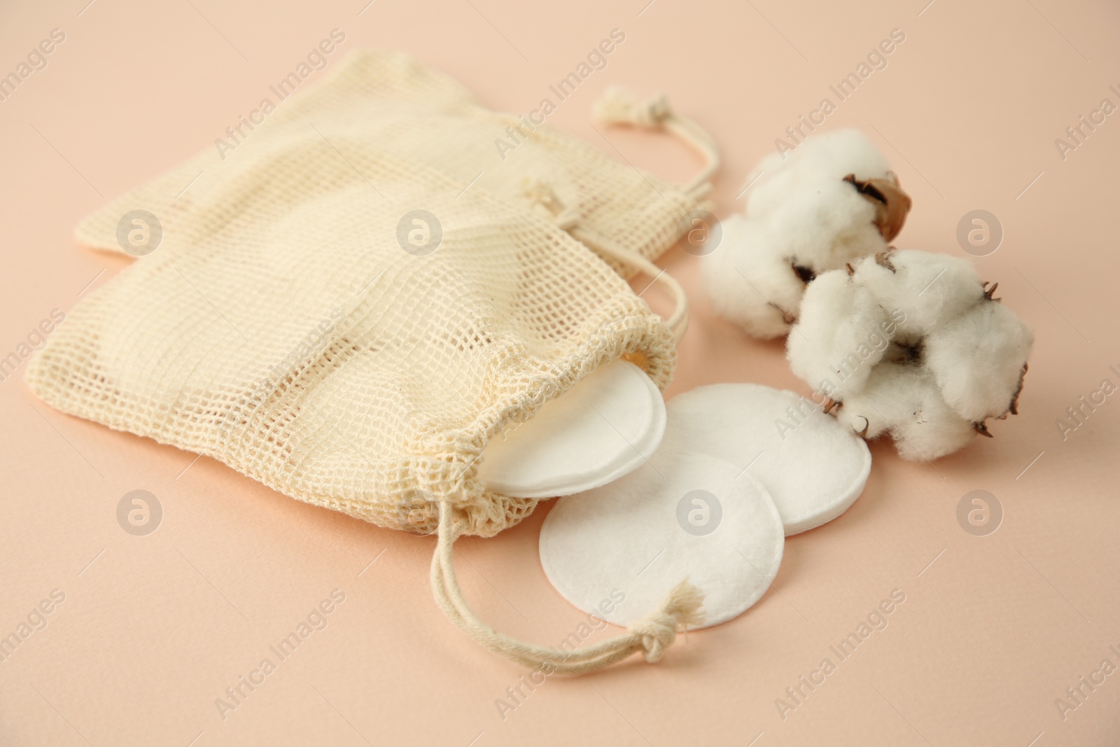 Photo of Bags with cotton pads and flowers on beige background, closeup