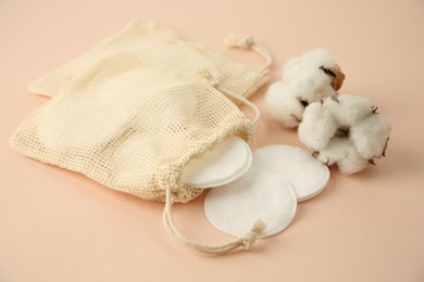 Bags with cotton pads and flowers on beige background, closeup