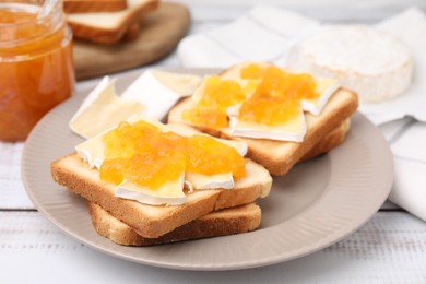 Tasty sandwiches with brie cheese and apricot jam on white wooden table, closeup