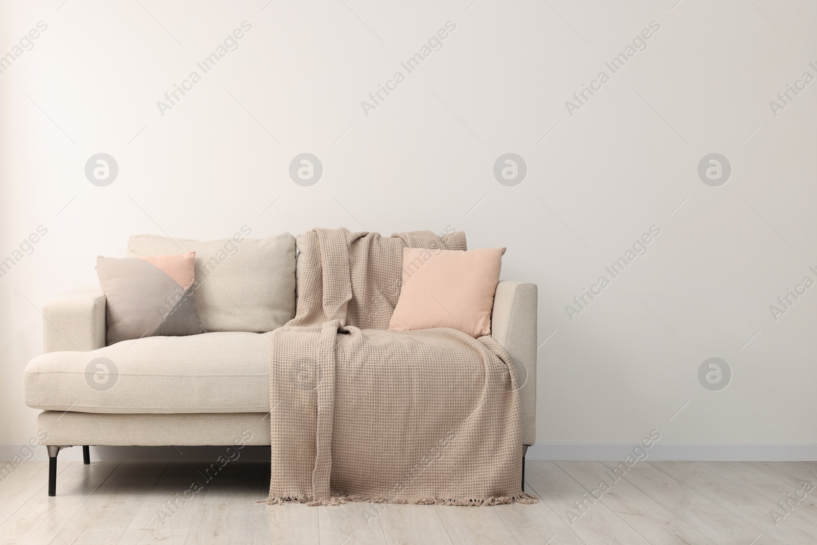 Photo of Cozy sofa with pillows and blanket in living room, space for text. Interior design