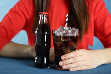Woman with glass and bottle of cola at blue table, closeup. Refreshing soda water