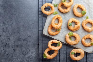 Cooling rack with fried onion rings on grey background, top view