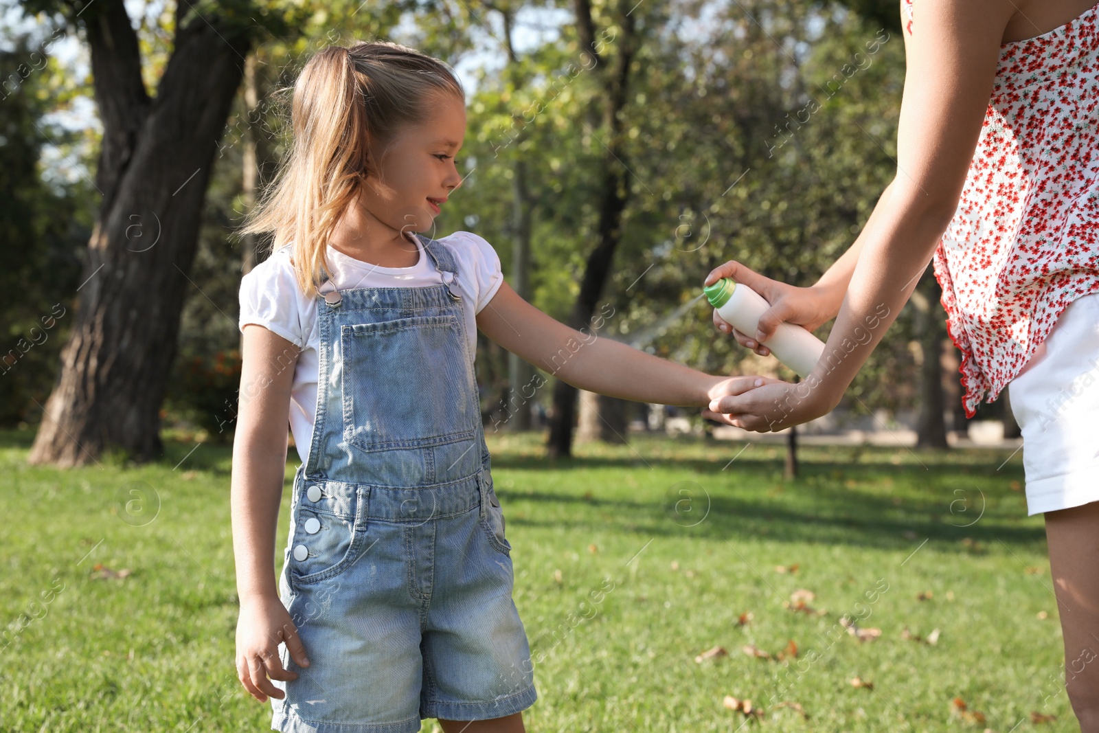 Photo of Mother applying insect repellent onto girl's hand in park