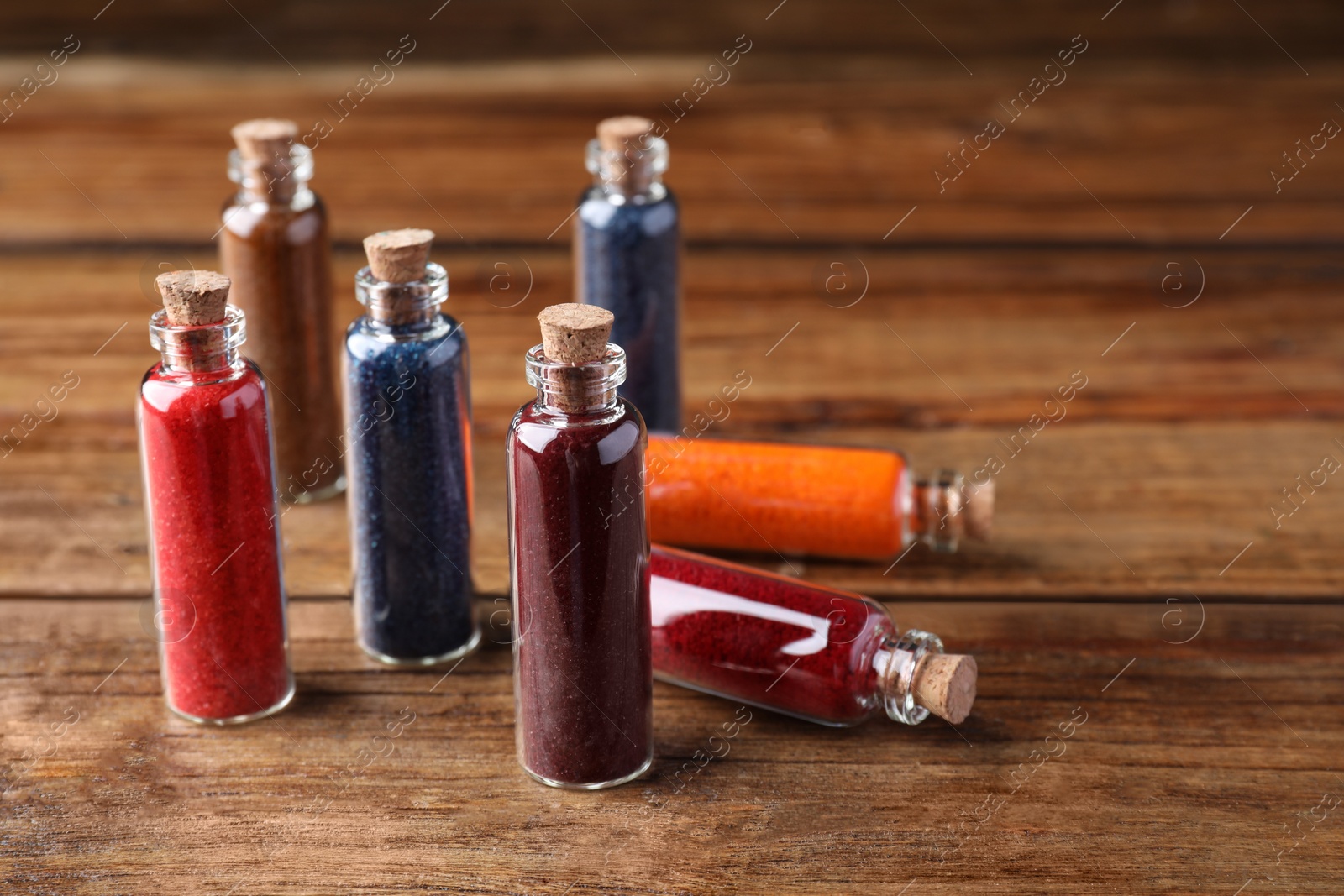 Photo of Glass bottles with different food coloring on wooden table. Space for text