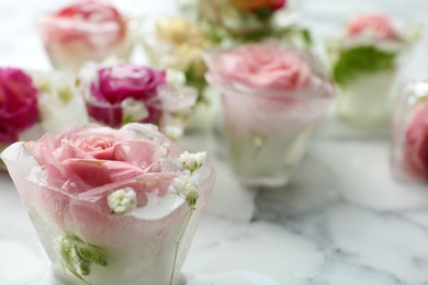 Photo of Ice cubes with flowers on marble background, closeup. Space for text