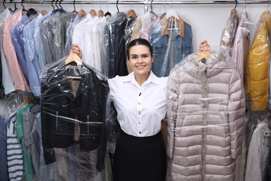 Photo of Dry-cleaning service. Happy worker with clothes in plastic bags indoors