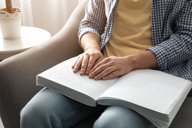 Photo of Blind man reading book written in Braille on sofa, closeup