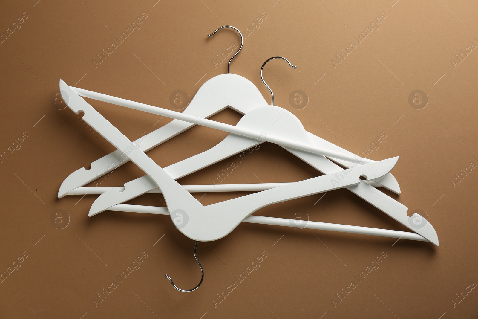 Photo of White hangers on brown background, top view