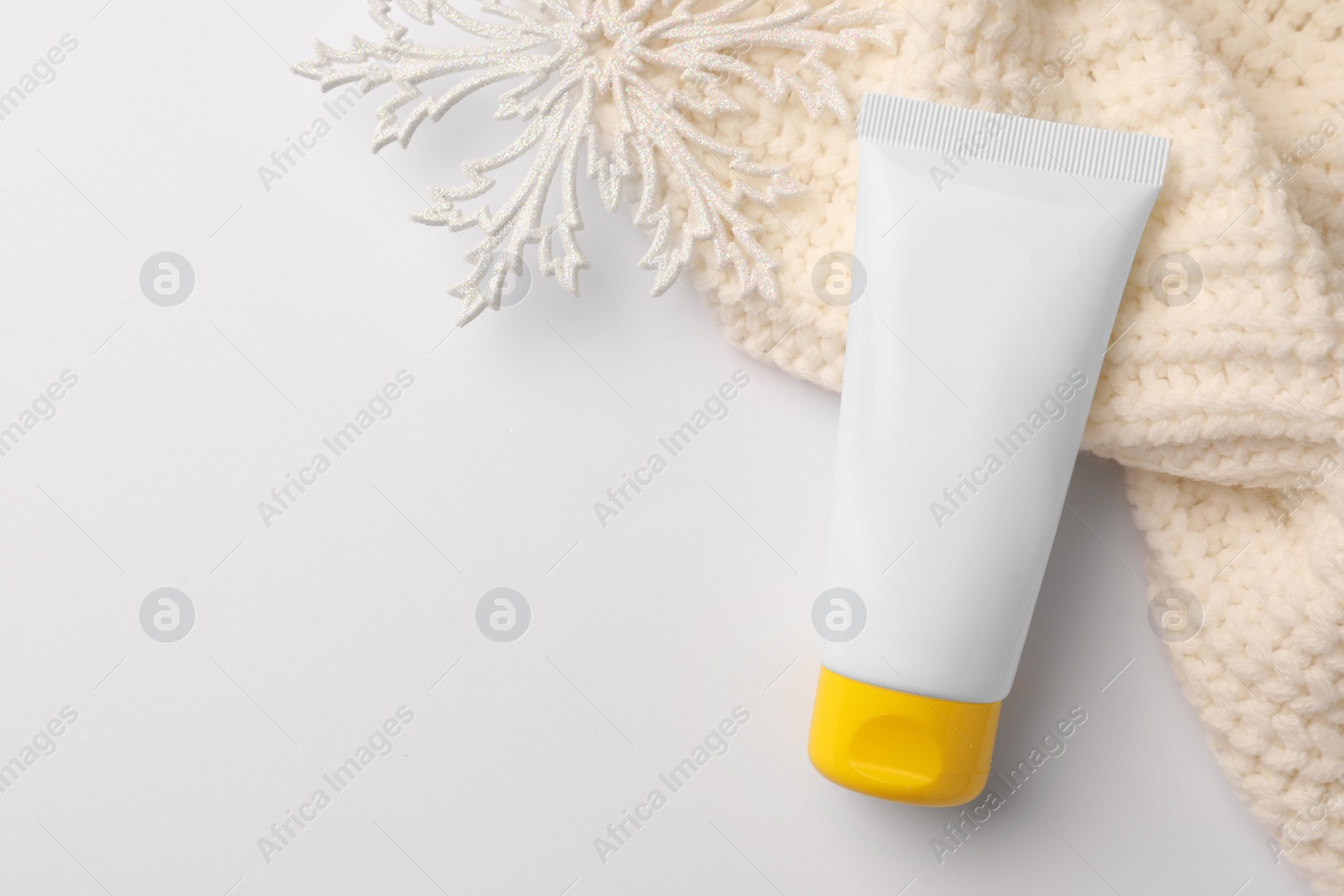 Photo of Winter skin care. Hand cream, decorative snowflake and knitted sweater on white background, top view. Space for text