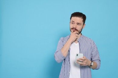 Photo of Pensive man with smartphone against light blue background. Space for text