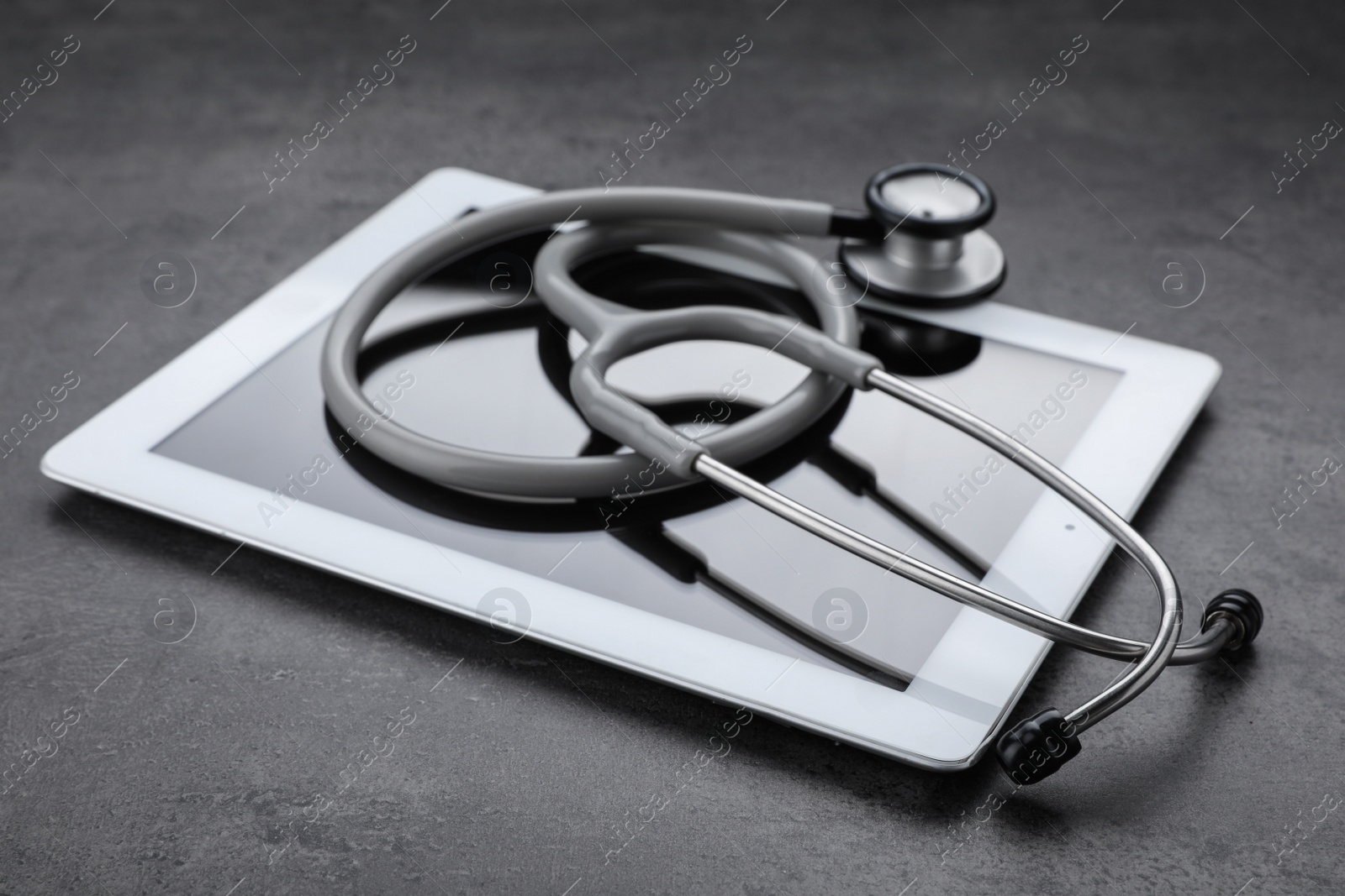 Photo of Computer tablet with stethoscope on grey table, closeup