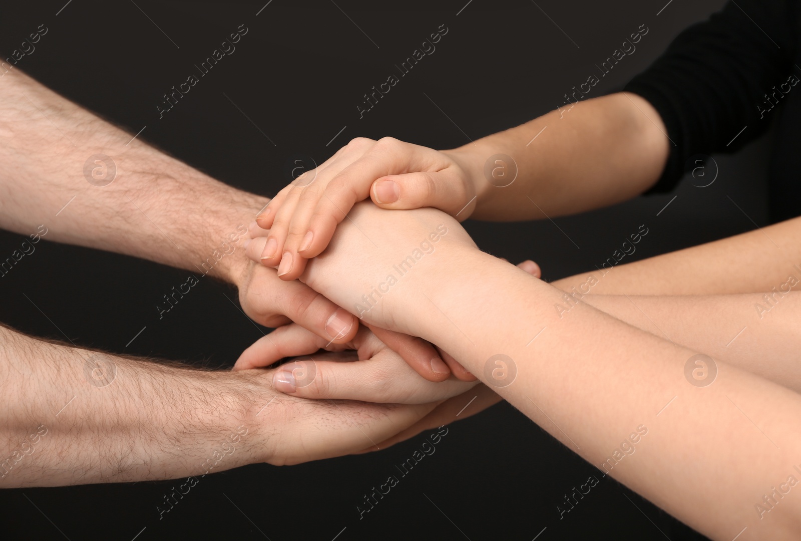 Photo of Young people putting their hands together on dark background, closeup