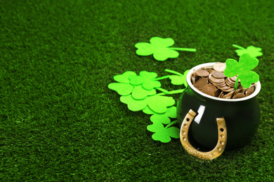 Photo of Pot of gold coins, horseshoe and clover leaves on green grass, space for text. St. Patrick's Day celebration