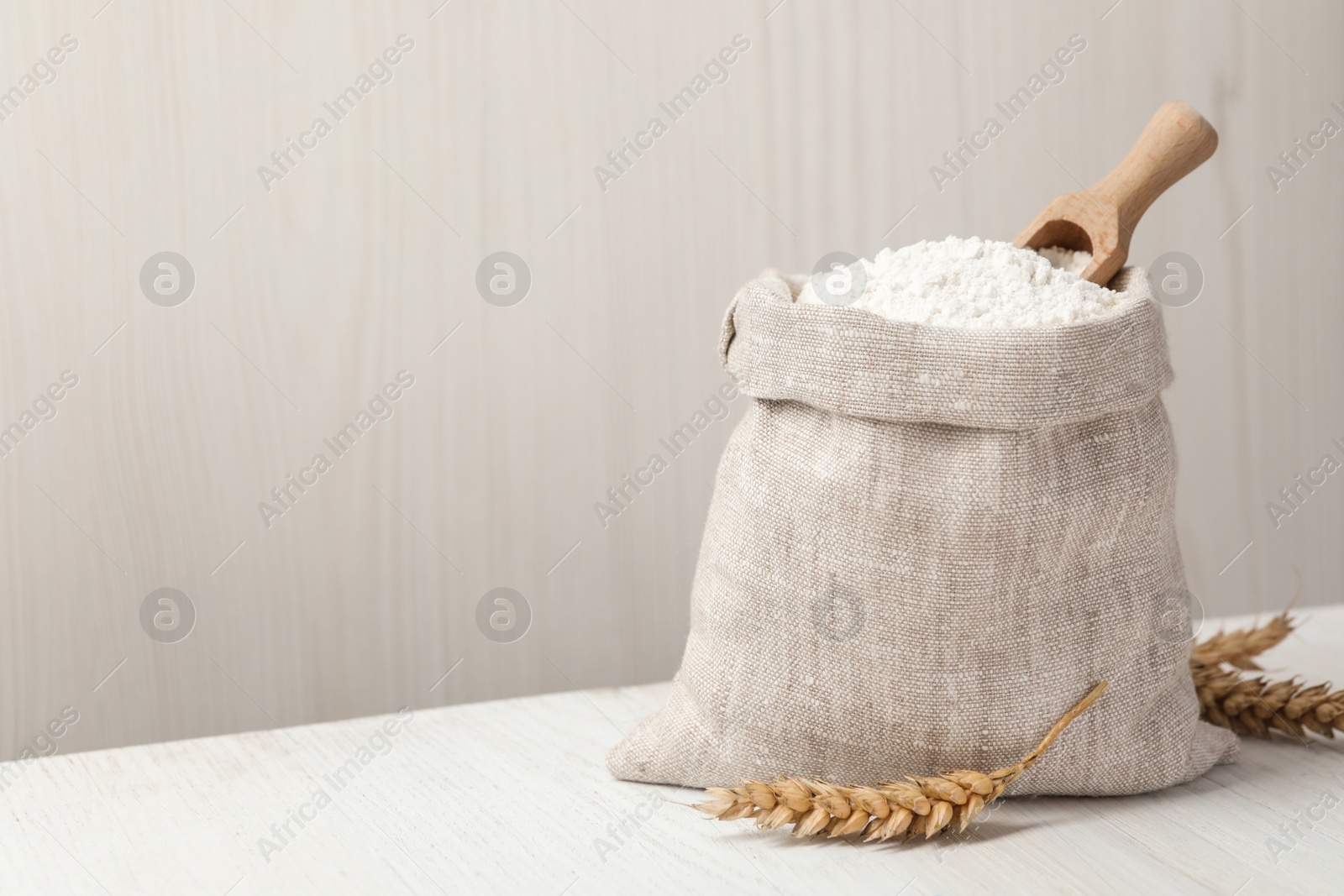 Photo of Wheat flour and spikelets on white table. Space for text