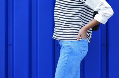 Photo of Young hipster woman in stylish jeans posing near color wall