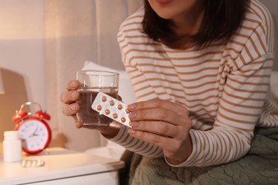 Photo of Woman with glass of water and pills suffering from insomnia in bedroom at night, closeup