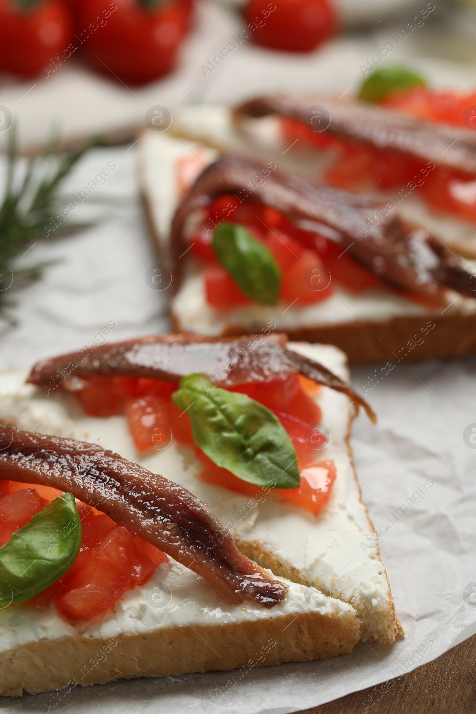 Photo of Delicious sandwiches with cream cheese, anchovies, tomatoes and basil on wooden board, closeup