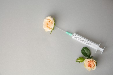 Photo of Medical syringe and beautiful roses on grey background, flat lay. Space for text