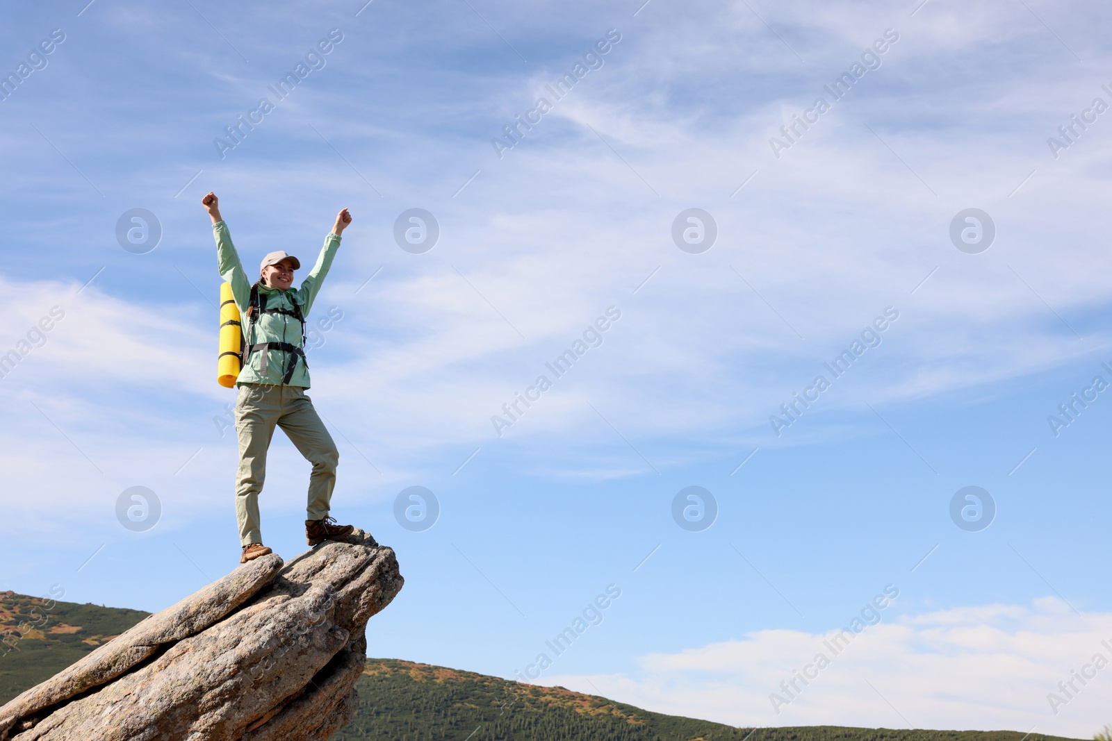 Photo of Young woman with backpack and sleeping mat on cliff in mountains. Space for text