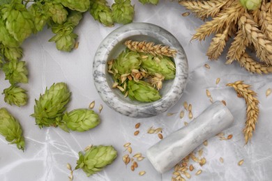 Photo of Mortar with pestle, fresh hops and ears of wheat on light grey marble table, flat lay
