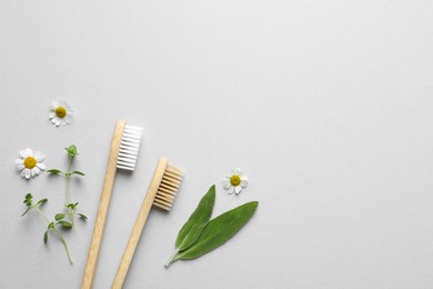 Bamboo toothbrushes, beautiful chamomile flowers and herbs on white background, flat lay. Space for text