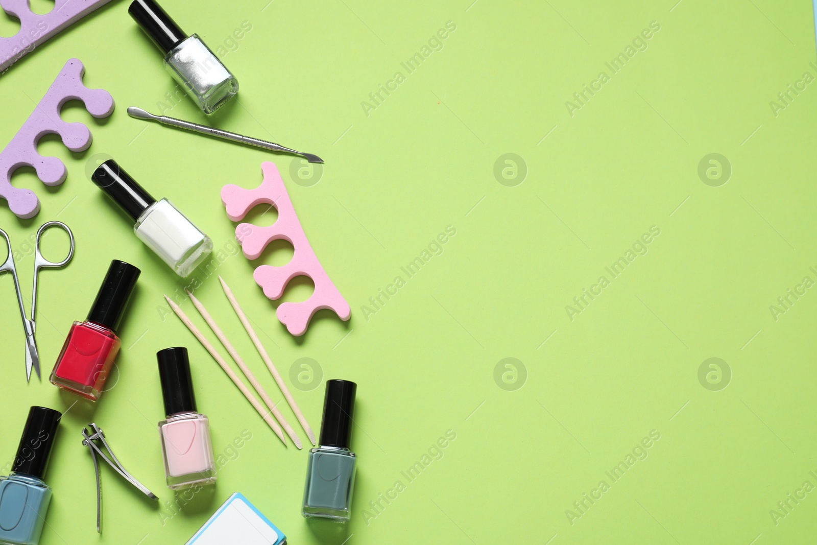 Photo of Nail polishes and set of pedicure tools on green background, flat lay. Space for text