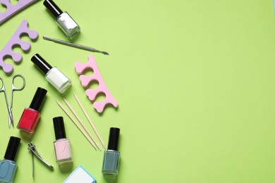 Photo of Nail polishes and set of pedicure tools on green background, flat lay. Space for text