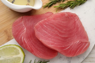 Raw tuna fillets with rosemary, lime and oil on board, top view