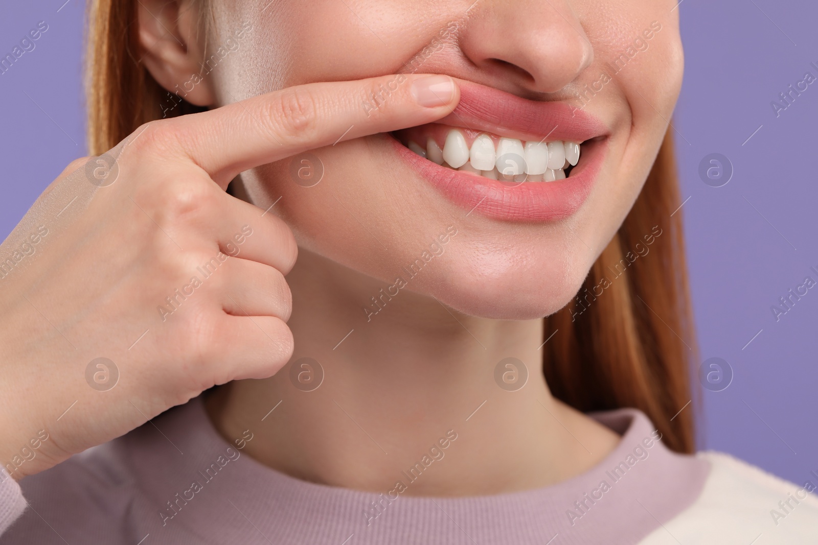 Photo of Woman showing her clean teeth on violet background, closeup