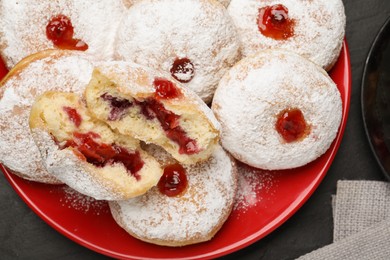Delicious donuts with jelly and powdered sugar on black table, closeup