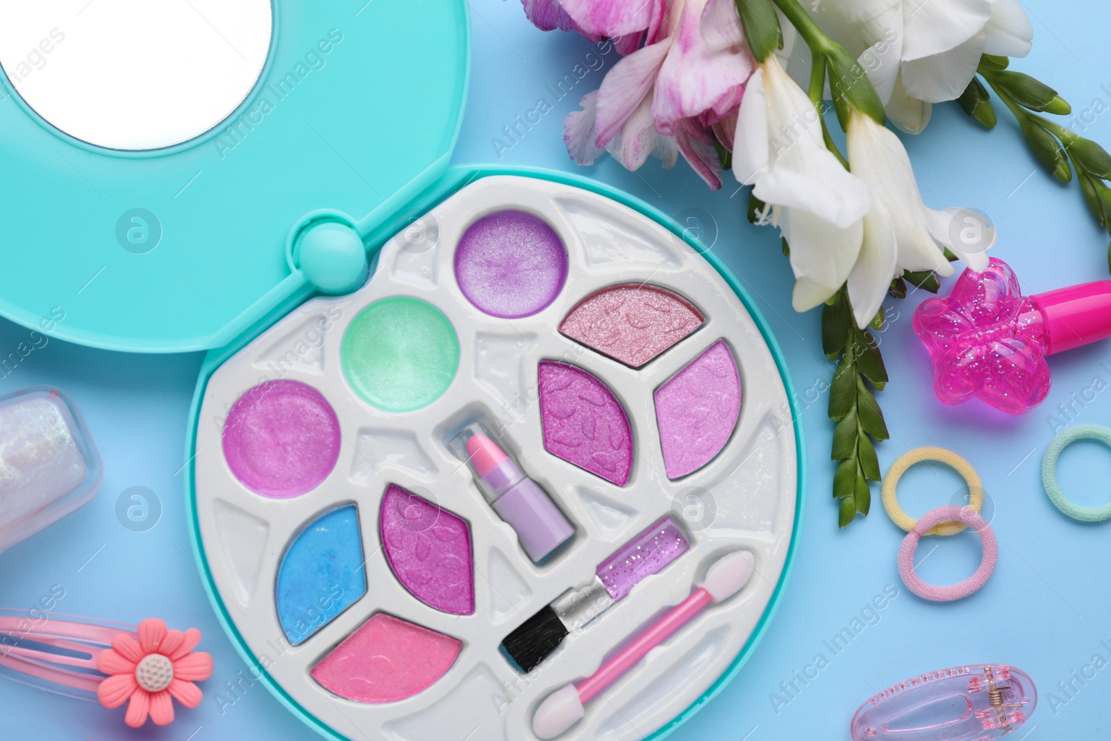 Photo of Decorative cosmetics for kids. Eye shadow palette, accessories and flowers on light blue background, flat lay
