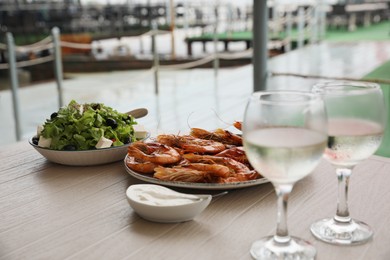 Photo of Delicious cooked shrimps served with glasses of white wine on wooden table outdoors