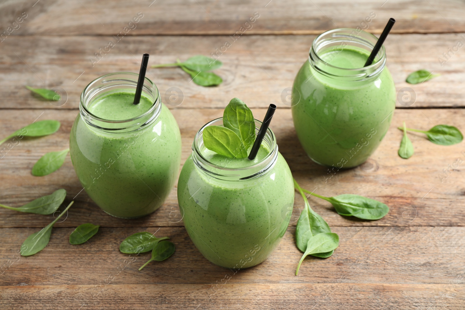 Photo of Jars of healthy green smoothie with fresh spinach on wooden table