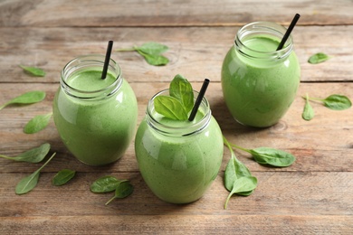 Photo of Jars of healthy green smoothie with fresh spinach on wooden table