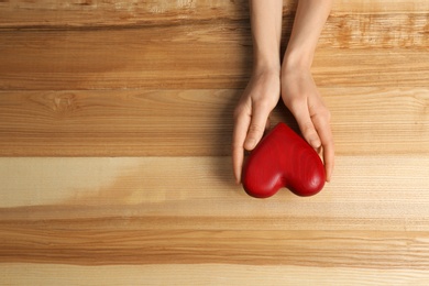 Woman holding decorative heart on wooden background, top view. Space for text